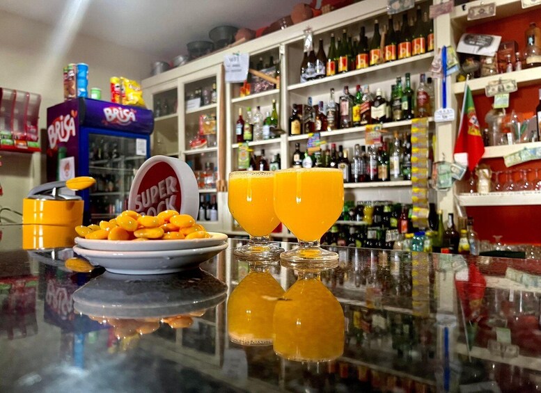 A bar counter with two glasses of orange juice, a bowl of snacks, and shelves stocked with various bottles. 5