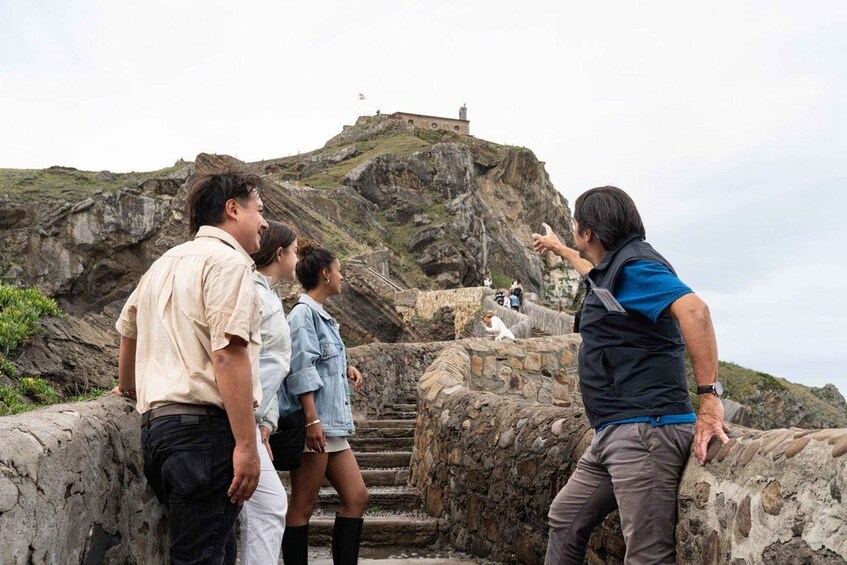 A group of people standing on a rocky outcrop overlooking a fort on a hill. 3