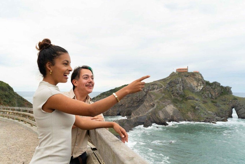 A couple on a coastal road overlooking a rugged coastline with a prominent cliff and a building on top. 5