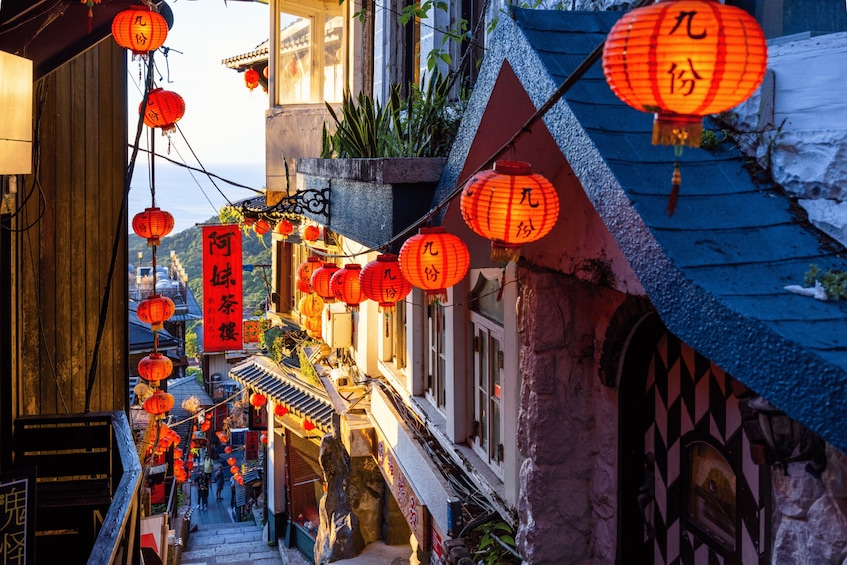 A narrow street with traditional buildings, red lanterns, and a sign with Chinese characters. 1