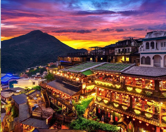 A traditional village at dusk with illuminated buildings and a mountain in the background. 2