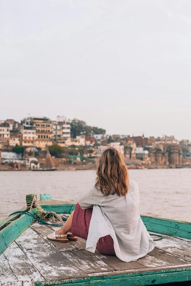 A person sitting on a wooden boat with a cityscape in the background. 5