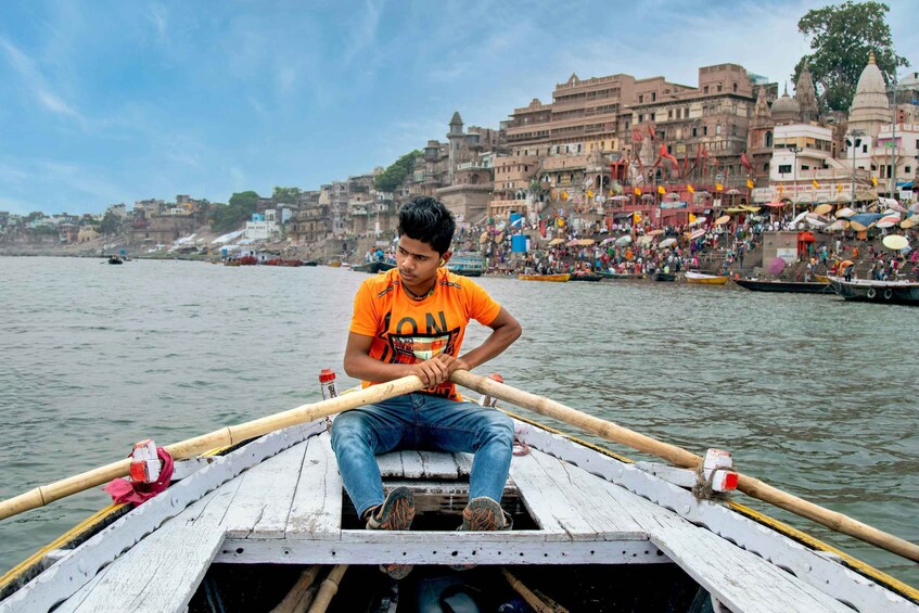 A person rowing a boat on a river with a densely populated riverside in the background. 2