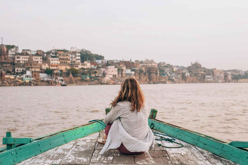 A person sitting on a wooden boat with a cityscape in the background. 1