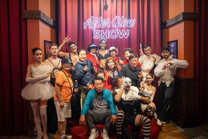 A group of people posing in front of a neon sign that reads "After Glow SHOW" in a theater setting. 2