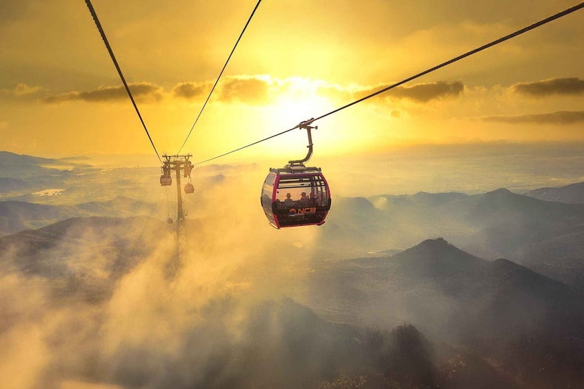 A cable car system with a cable car in the foreground and another in the background, set against a backdrop of mountains and a setting sun. 3