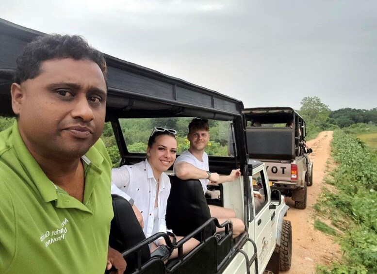 Three people in a safari vehicle on a dirt path surrounded by greenery. 2