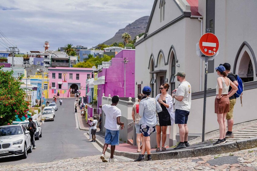 A colorful street with people standing on the sidewalk, a no entry sign, and a building with arched windows. 1