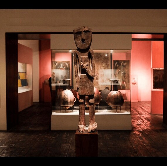 A sculpture in a museum with a red-lit background and pottery on display. 4