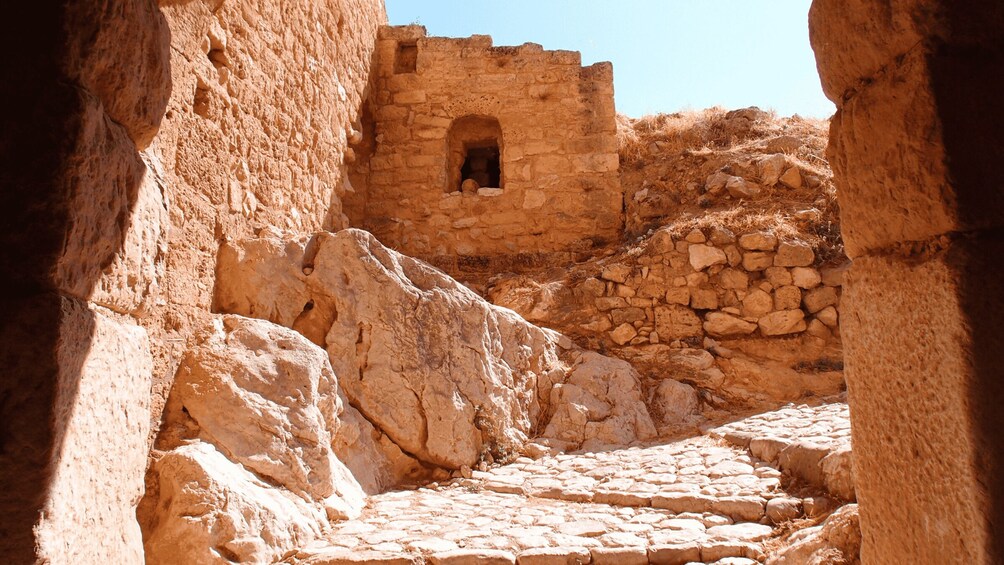 An ancient stone pathway leading through a fortified structure with arched openings and rugged walls. 3
