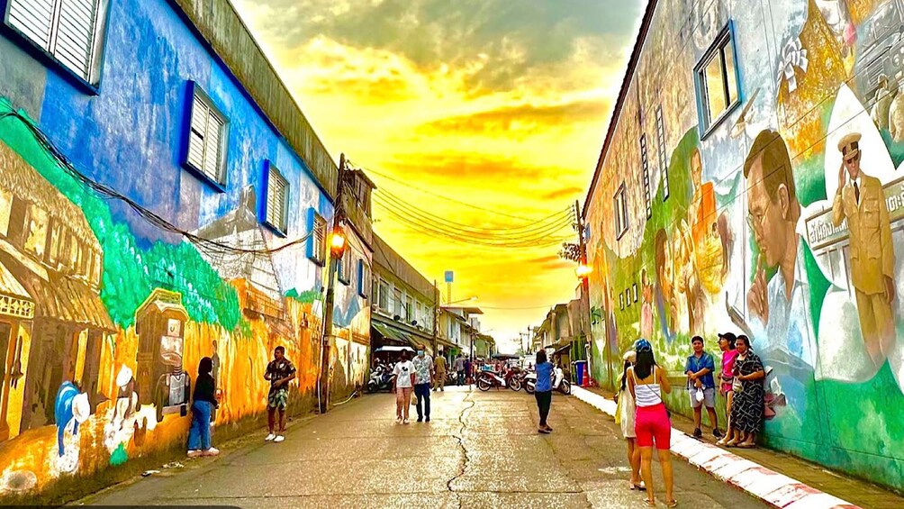 A street with colorful murals, pedestrians, and a sunset sky. 2