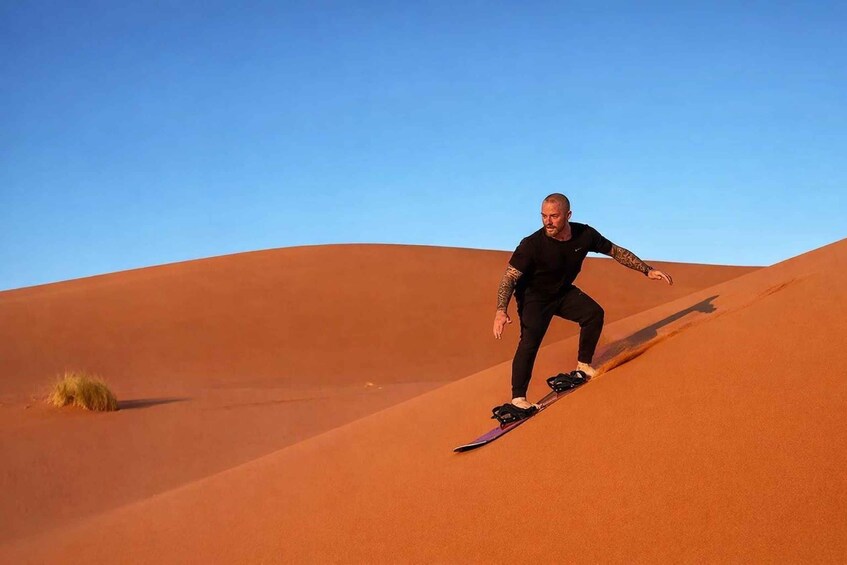 A person riding a board on a sand dune. 5