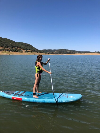 A person paddleboarding on a calm lake with hills in the background. 4