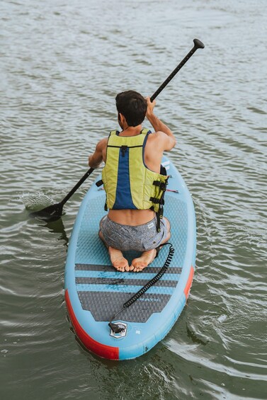 A person sitting on a paddleboard in the water, wearing a life jacket and holding a paddle. 1