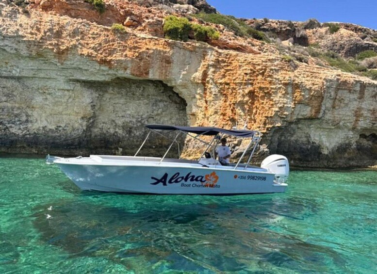 A boat named 'Aloha Boat Charter Malta' on clear turquoise water with rocky cliffs in the background. 2