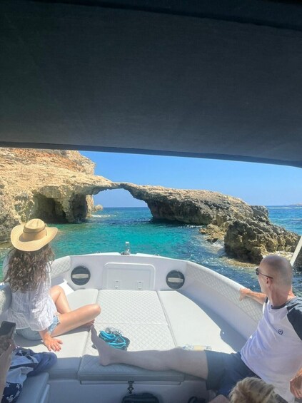 A boat with two people, one wearing a hat, and a rocky arch formation in the background. 4