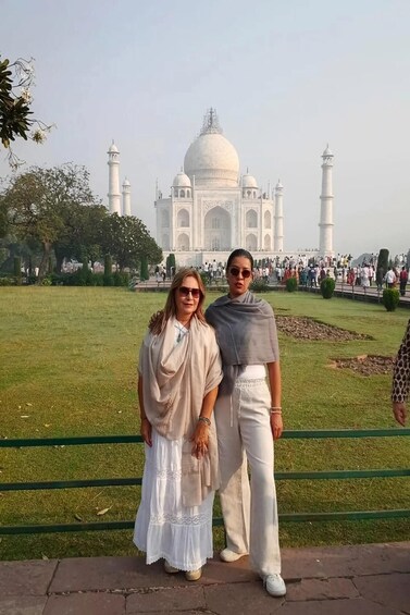 Two people standing in front of the Taj Mahal with its four minarets visible. 3