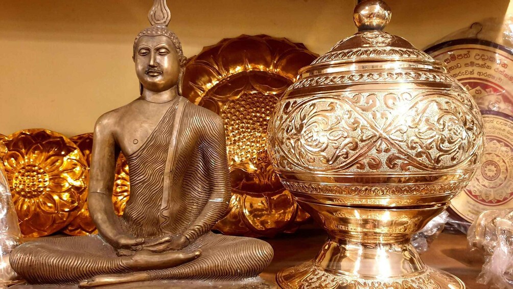 A seated Buddha statue next to ornate golden bowls. 2
