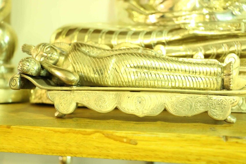 A detailed silver statue of a reclining figure on a decorative stand. 3