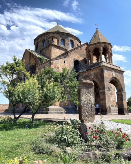 A historic stone church with a central dome and a bell tower, surrounded by a well-maintained garden with flowering plants. 5