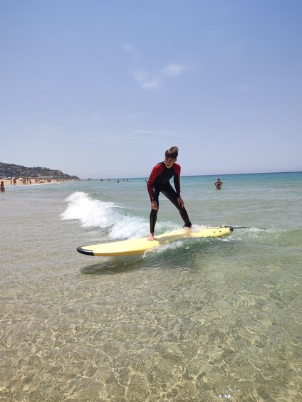 A person surfing on a yellow board in clear shallow water. 1