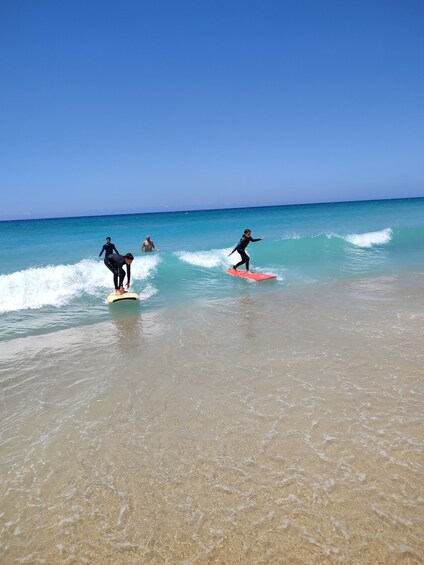 Three people surfing on a beach with clear blue water and a calm sea. 4