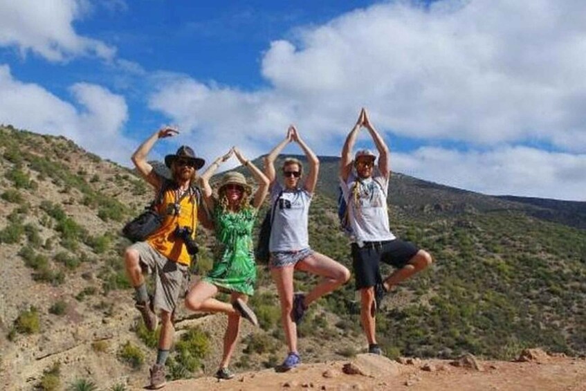Four people posing on a rocky hillside with their arms raised. 3