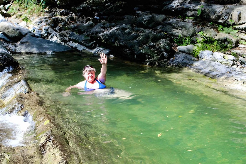 A person swimming in a clear, rocky stream surrounded by greenery. 2