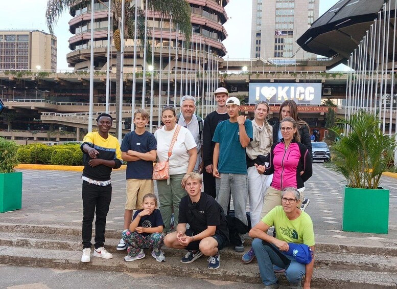 Eine Gruppe von Personen posiert vor einem Gebäude, an dem ein Schild mit der Aufschrift 'I ♥ KICC' befestigt ist. 2