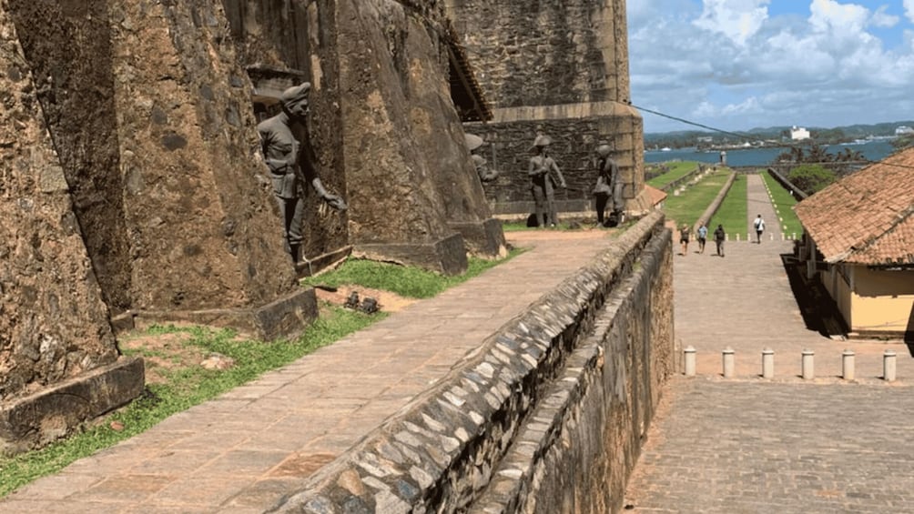 A stone pathway leading to a large fortress with statues and a view of a lake. 3