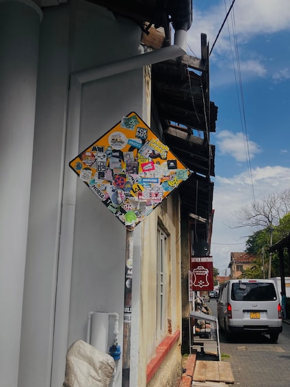 A street corner with a sign covered in various stickers, a parked van, and a building with a red brick base. 5