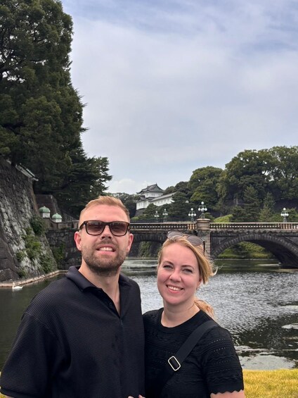 A man and a woman standing in front of a historic bridge with a castle in the background. 2