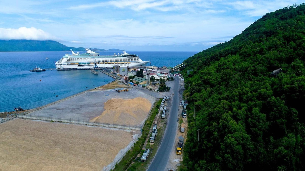A large cruise ship docked at a port with a forested hillside in the background. 5