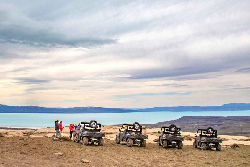 Four off-road vehicles parked on a grassy area with a lake and mountains in the background. 5