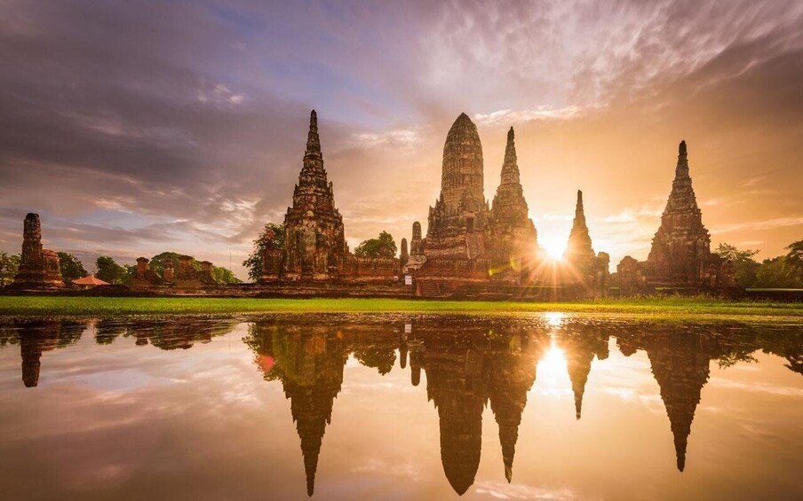 A temple complex with multiple tall spires, reflecting in a calm body of water, with the sun setting in the background. 1