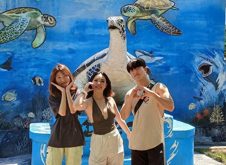 Three people posing in front of a mural with sea turtles and sharks. 1