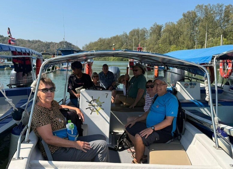 A group of people on a boat with a blue canopy, water in the background, and trees. 2