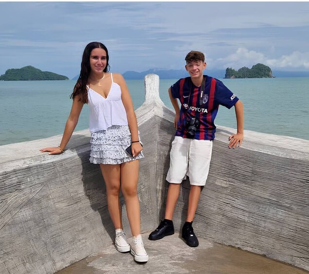 Two people standing on a concrete pier with a body of water and islands in the background. 1