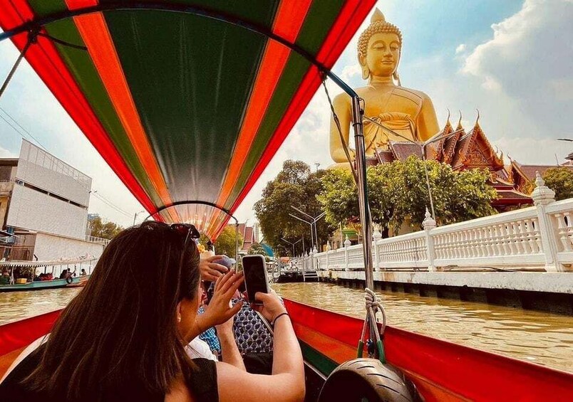 En stor, gylden Buddha-statue, en båd med rødt og grønt markise, og traditionel thailandsk arkitektur i baggrunden. 1