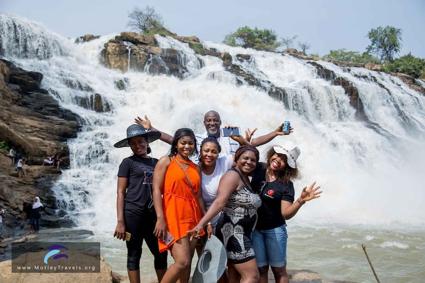 A group of people standing in front of a waterfall with a rocky landscape in the background. 5