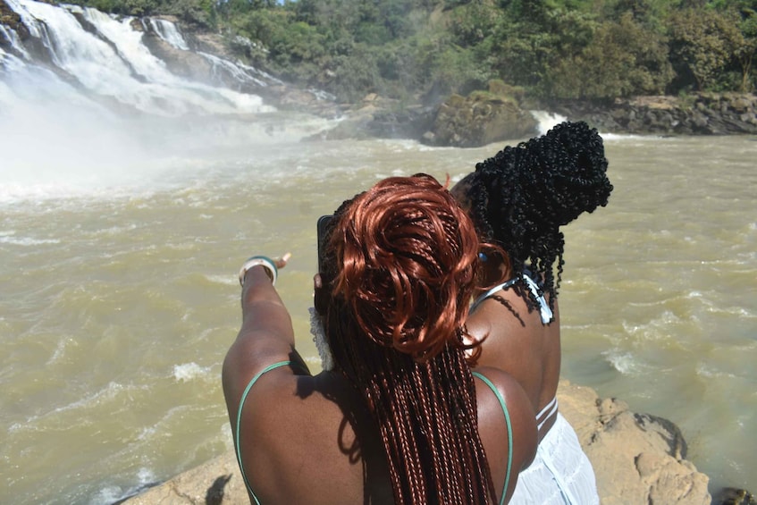 A person with braided hair standing by a waterfall. 4
