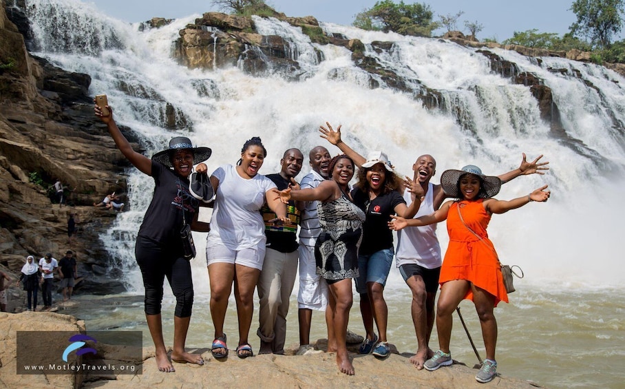 A group of people posing in front of a waterfall. 1