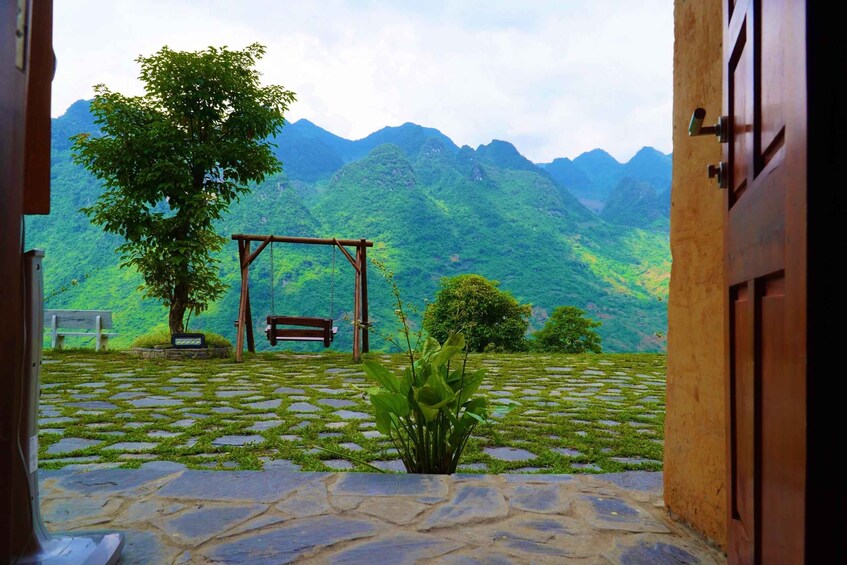 A stone pathway leading to a wooden swing set and bench, surrounded by lush greenery and mountains. 5