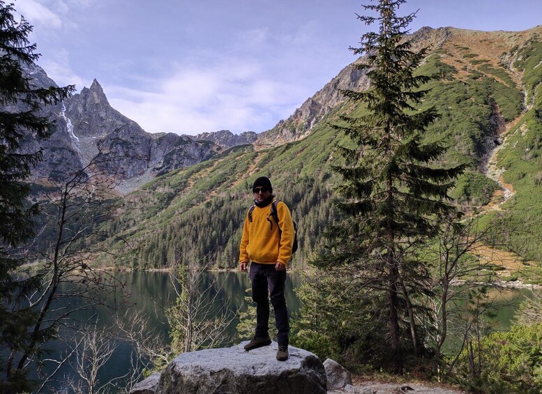 A person standing on a rock by a lake with mountains in the background. 5