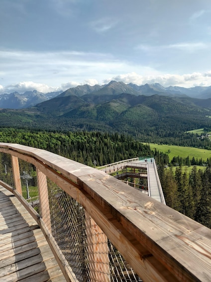 A wooden observation deck overlooking a mountainous landscape with a forested valley and distant peaks. 4