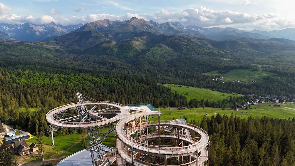 A circular observation tower with a spiral walkway, surrounded by dense forest and mountains in the background. 2