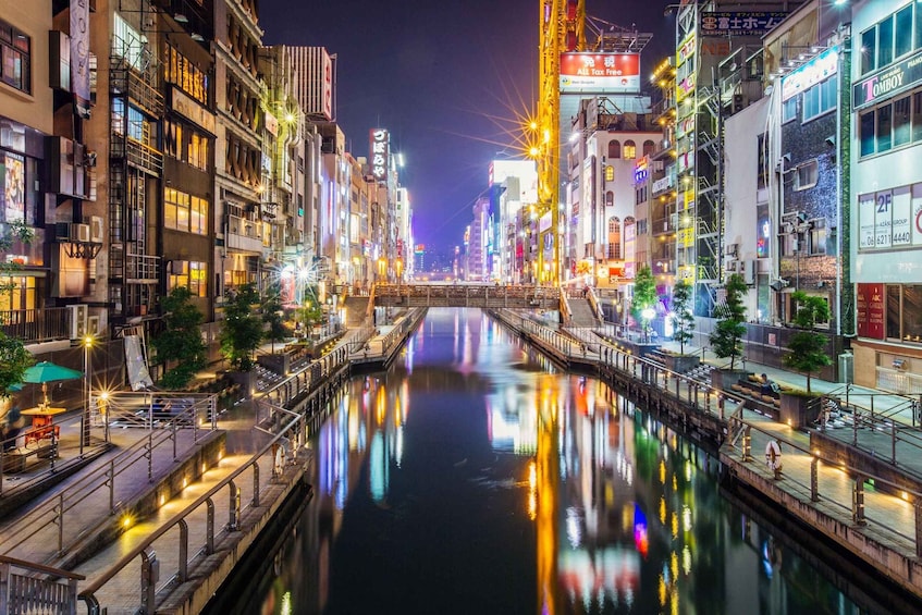 A nighttime view of a river with reflections of city lights, surrounded by buildings with illuminated signs. 5