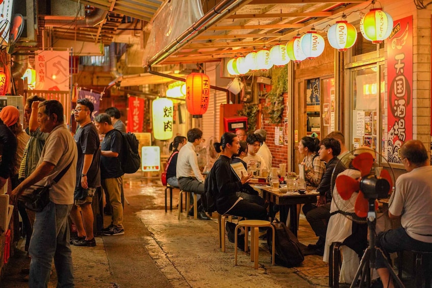 A bustling street scene with people dining at outdoor tables, illuminated by traditional lanterns. 1