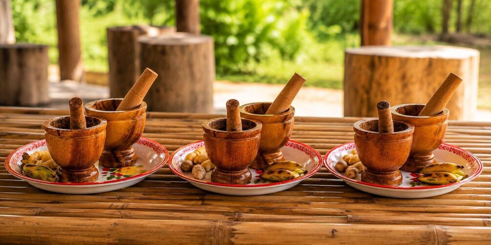 Wooden mortars with pestles on plates, surrounded by bananas and plantains. 5