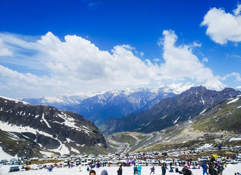 A mountainous landscape with snow-covered peaks, a valley, and a gathering of people and vehicles at the base. 4